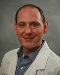 A professional headshot of Matthew Deibel in light blue attire against a gray background.