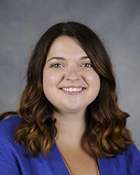 Professional headshot of Alexis Hadaway in dark blue attire against a gray background.