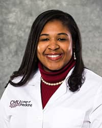 A woman with long, black hair and a maroon blouse wears a white coat and smiles for a headshot.
