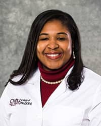 A woman with long, black hair and a maroon blouse wears a white coat and smiles for a headshot.