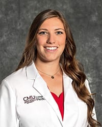 A woman with long, dark hair and a red blouse wears a white coat and smiles for a headshot.