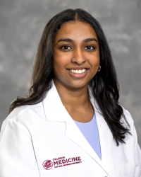 Bommineni, Maanasa_student_200x250 A woman with long dark hair smiles while wearing a white medical coat embroidered with