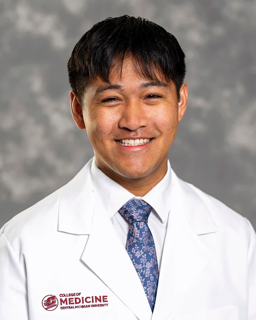 A male CMU College of Medicine medical student wearing his white coat as he smiles for the camera.