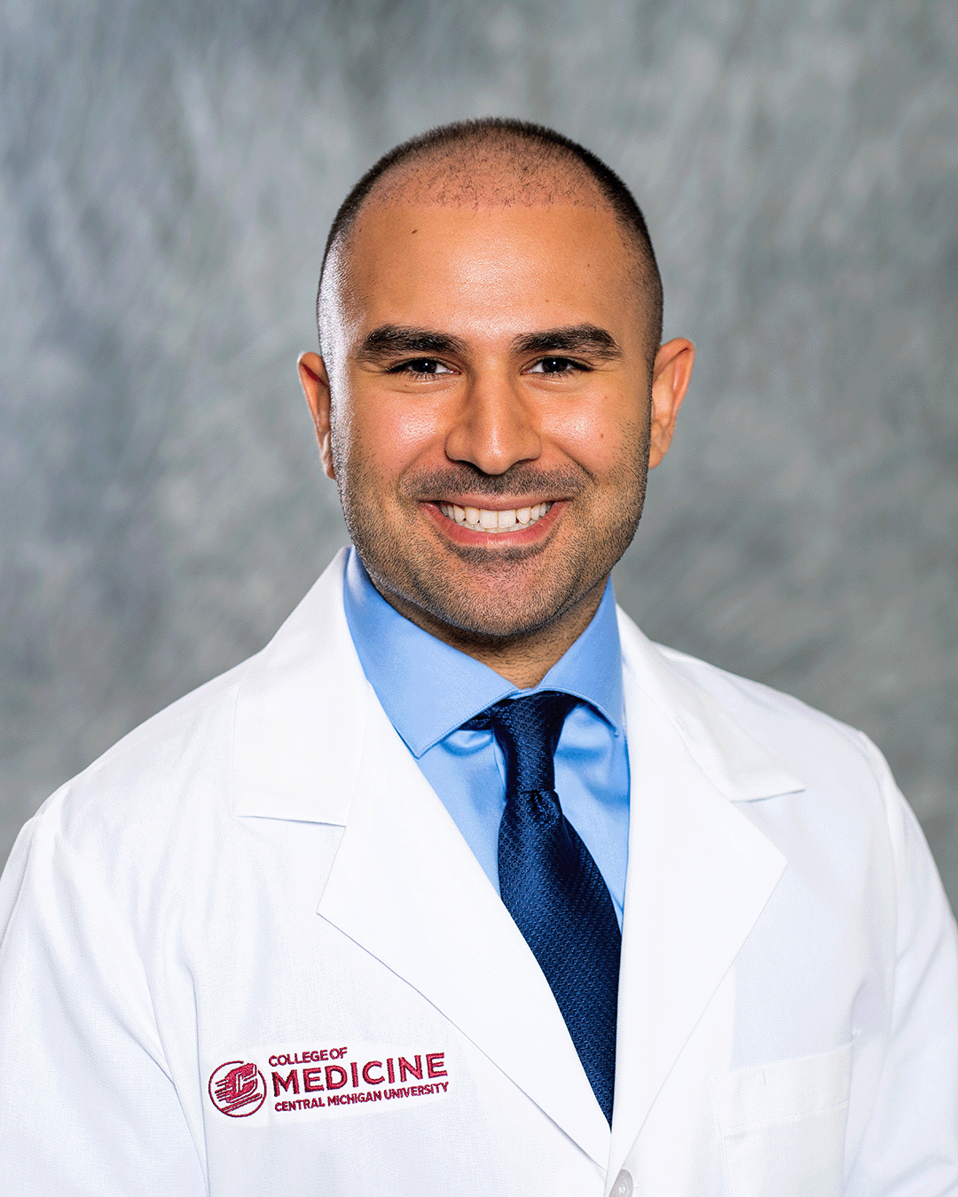 A male CMU College of Medicine medical student wearing his white coat as he smiles for the camera.