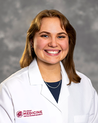 A female medical student in a white lab coat embroidered with a Central Michigan University College of Medicine logo.