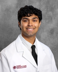 Kothari, Tej_student_200x250 A young man with short, curly hair wearing a white medical coat with