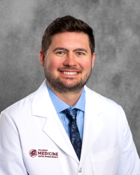 Smith, Brian 200x250 A man with short hair and a beard is wearing a white medical coat with