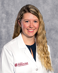 A female medical student in a white lab coat embroidered with a Central Michigan University College of Medicine logo.