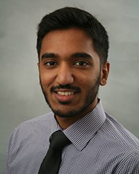 A professional headshot of Abishek Bala in dark attire against a gray background.