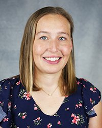 A professional headshot of Lindsay Davis in floral attire against a gray background.