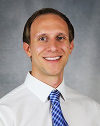 A professional headshot of Steven Hale in white attire against a gray background.