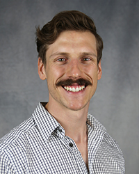 A professional headshot of Andrew Namespetra in light attire against a gray background.