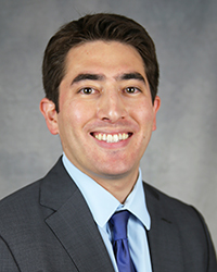 A professional headshot of Joshua Rarick in dark attire against a gray background.