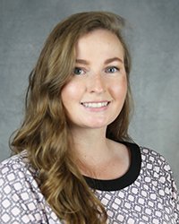 A professional headshot of Laura Schroeder in light attire against a gray background.