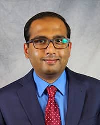 Headshot of Abdullah Islam wearing a blue suit with a blue shirt and a red necktie.