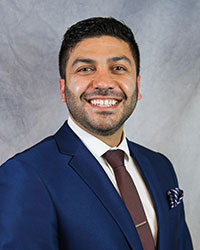 Headshot of Lahib Douda wearing a blue suit with a white dress shirt and brown necktie.