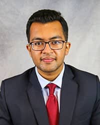 Headshot of George Matthew wearing a dark suit with a red tie.