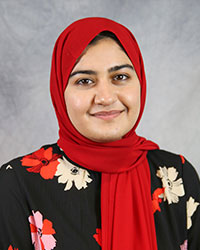 Headshot of Usheem Syed wearing a black floral print top and a red colored hijab covering around head and neck.