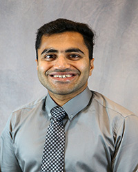 Headshot for Rahul Arora wearing a grey shirt and black and white checkered tie.