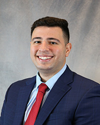 Headshot for Ramy Ballout wearing a blue blazer, blue shirt, and red tie.
