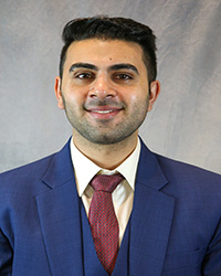 Headshot for Afrasayab Khan wearing a blue blazer, white shirt, and red tie.