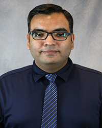 Headshot for Gaurav Luthra wearing a navy shirt and a blue striped tie.