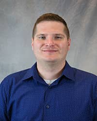 Headshot for Zachary Nine wearing a blue button-up shirt.