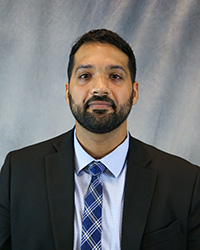 Headshot of Ishaan Sharma wearing a black blazer, light blue shirt, and blue patterned tie.