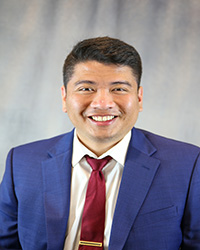 Headshot of Nhan Tran wearing a blue blazer, white top, and burgundy tie.