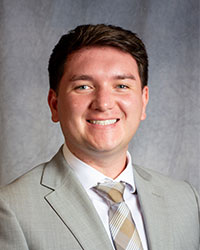 Tyler Firlik is wearing a grey suit coat and patterned tie.