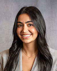 Sydney Pauls is wearing a grey blazer with long, dark hair.