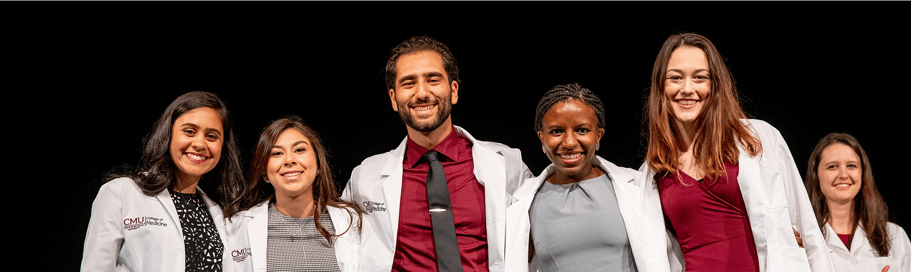 Medical students of varying genders and races standing together wearing white doctors' coats