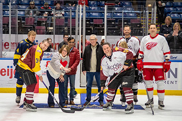 Five Hockey players and three people in plain clothes smile for the camera in a ceremonial puck drop