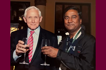 Two men in black jackets toast with wine glasses while smiling at the camera.