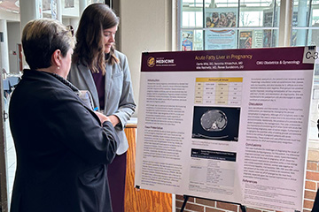 Two women in business attire look at a large poster displaying scientific research.