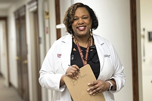 Dr. Pruitt wears a white lab coat and holds a clipboard to her chest as she smiles for the camera.