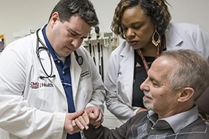 Dr. Pruitt and a man in a white lab coat inspect an older man.