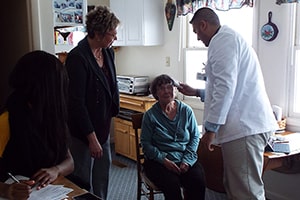 A man in a white lab coat checks the forehead of an older woman.