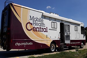 The side of a white RV that reads Mobile Health Central and has a burgundy and gold wave-like pattern.