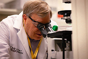 A man in a lab coat examines a specimen through a microscope in a laboratory setting.
