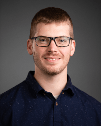 Man in blue button down shirt wearing glasses.