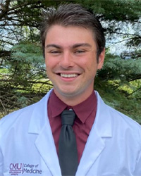 A man with short brown hair wearing a maroon shirt, black tie and CMU College of Medicine white lab coat smiles at the camera.