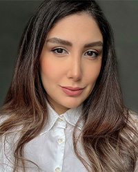 A woman with long brown hair wearing a white blouse smiles at the camera.