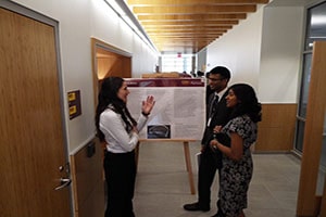 Young woman presenting her research poster to a man and woman.