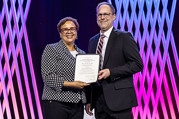 A woman with glasses and a man in a suit smile a the camera while displaying an award.