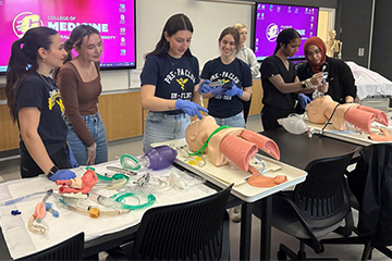 Six female students use simulation manikins to practice intubations while an instructor oversees.
