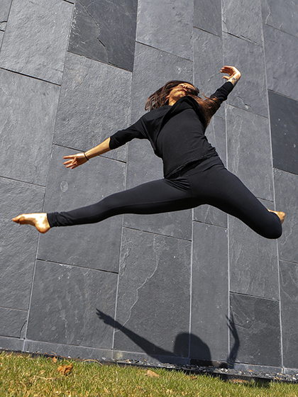 Student dancer leaping through the air in front of a brick wall.