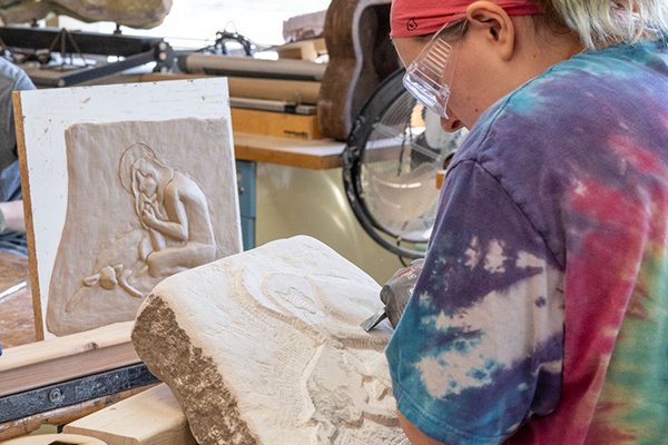 Art student is sculpting a design into stone with a chisel.