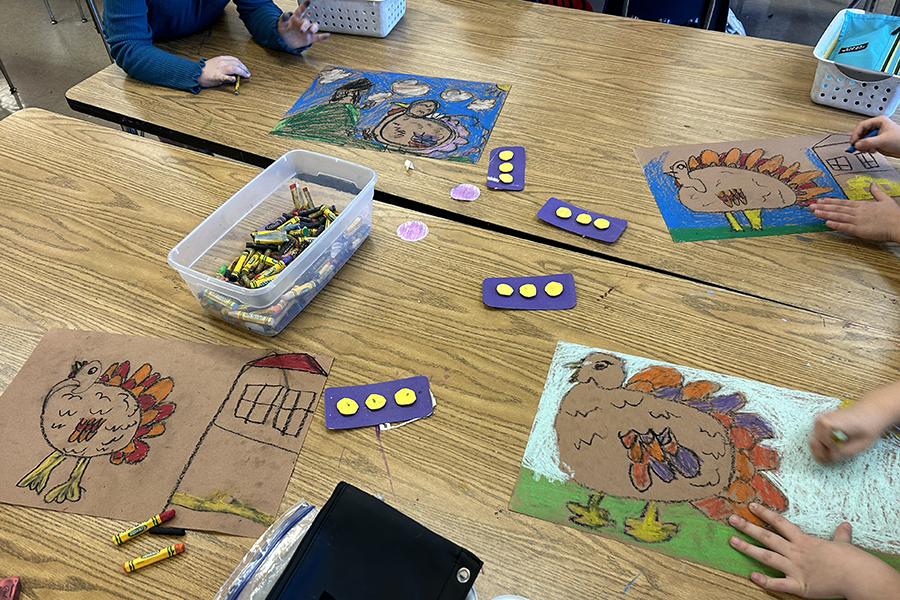 Tabletop in a classroom. Children are drawing pictures of turkeys with crayons.