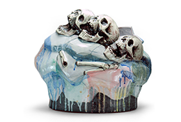 Ceramic sculpture. A multicolored base with three human skulls and a few scattered bones on top of it.